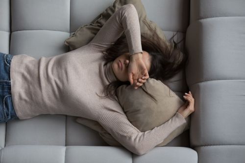 Exhausted woman lying down with her hand covering her face, representing hormone imbalance and fatigue